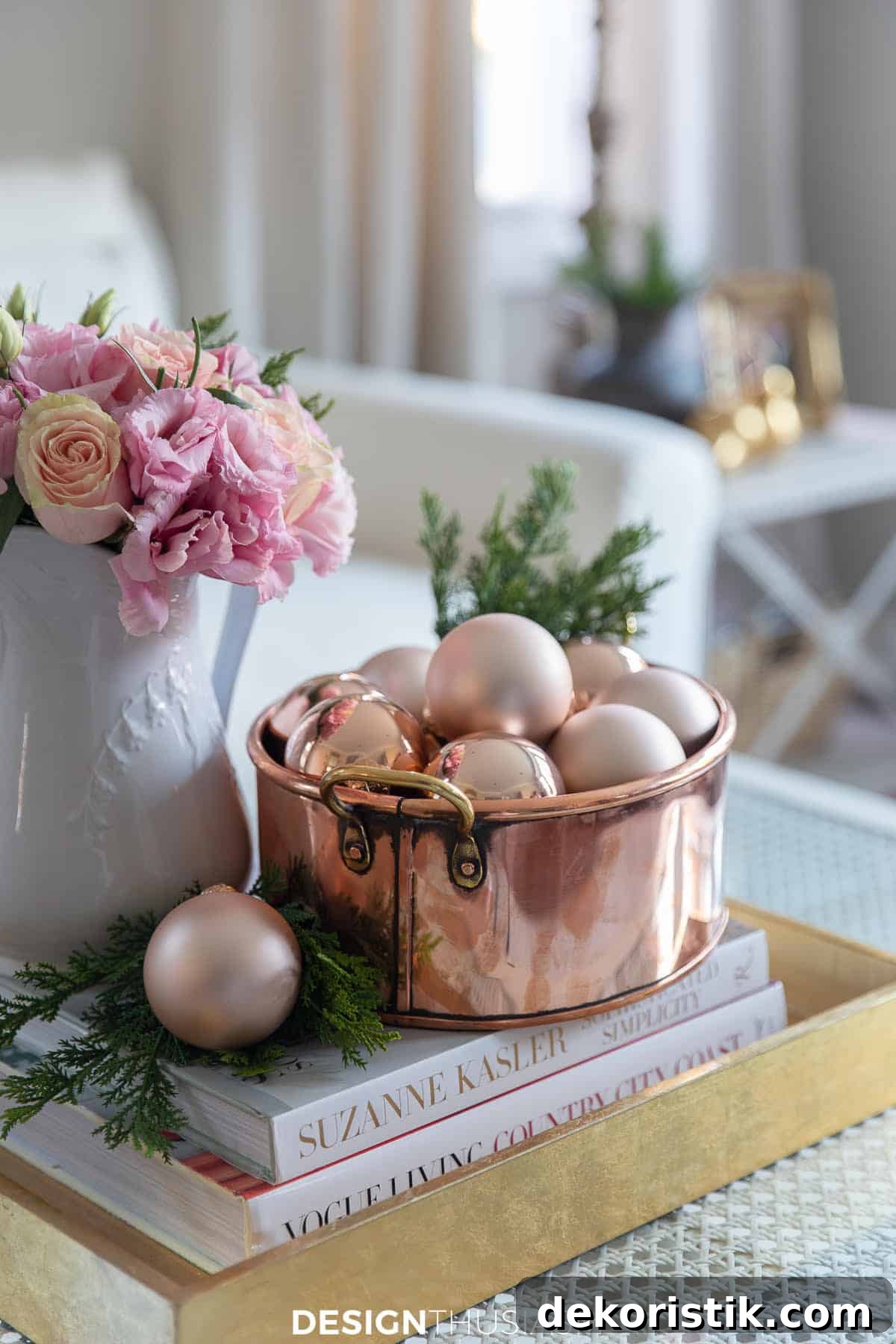 copper bowl filled with rose gold ornaments beside a vase of pink flowers