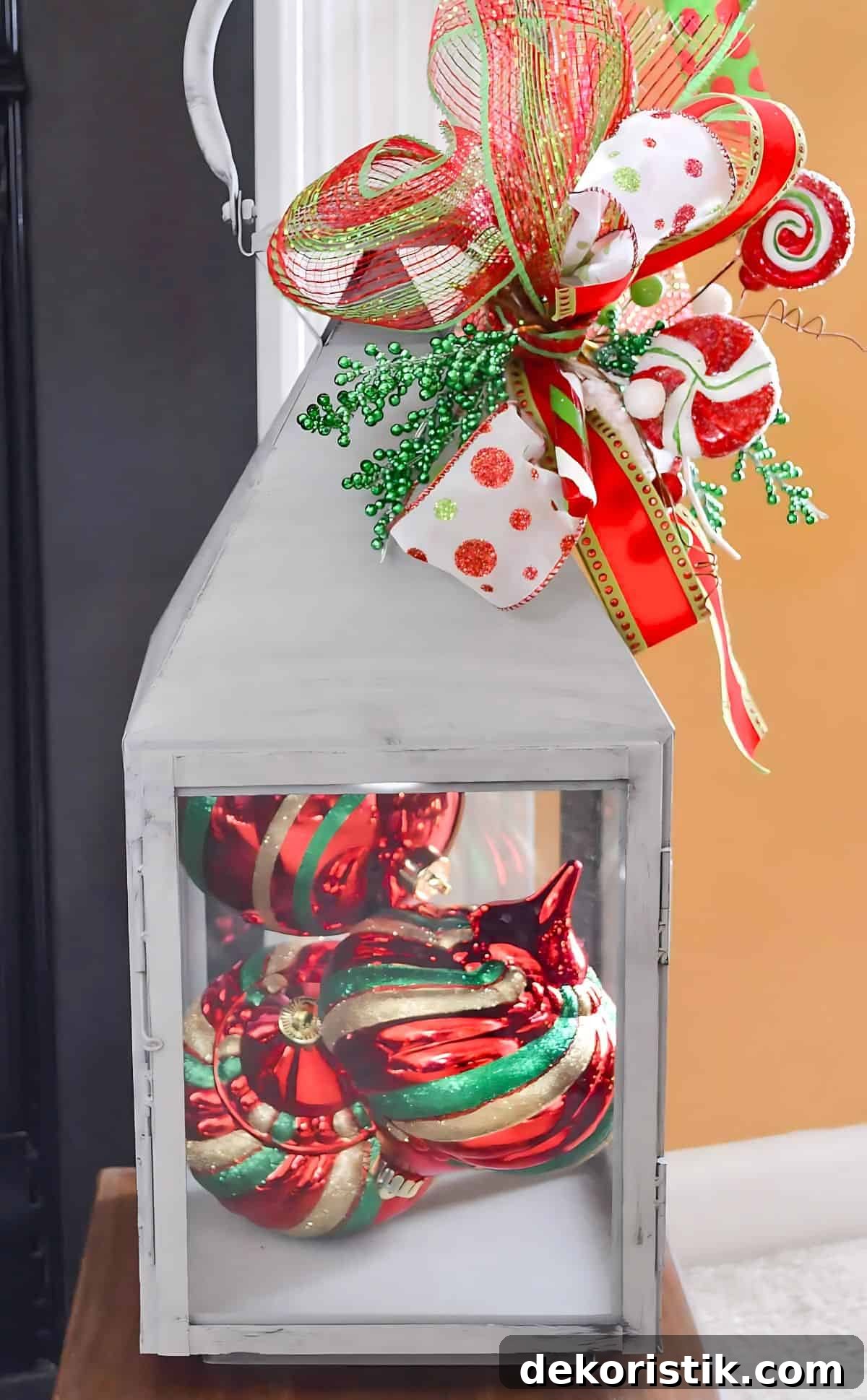 large lantern filled with red ornaments topped with a sparkly bow