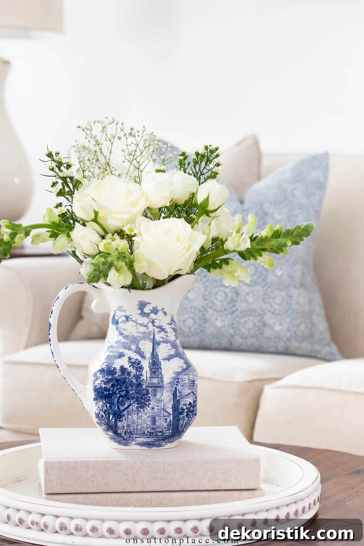 white flower arrangement in a blue and white pitcher on a coffee table