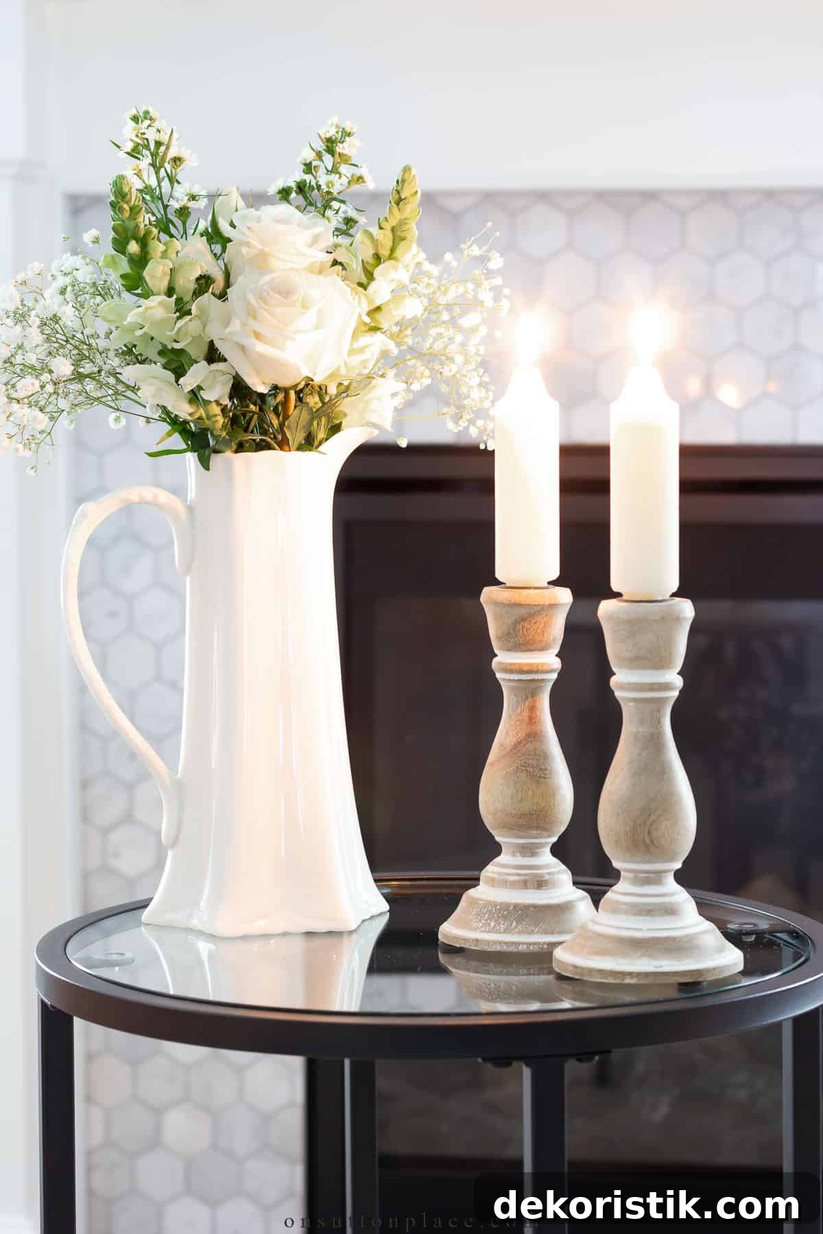 gray candlesticks with white candles and a white pitcher with white flowers in it