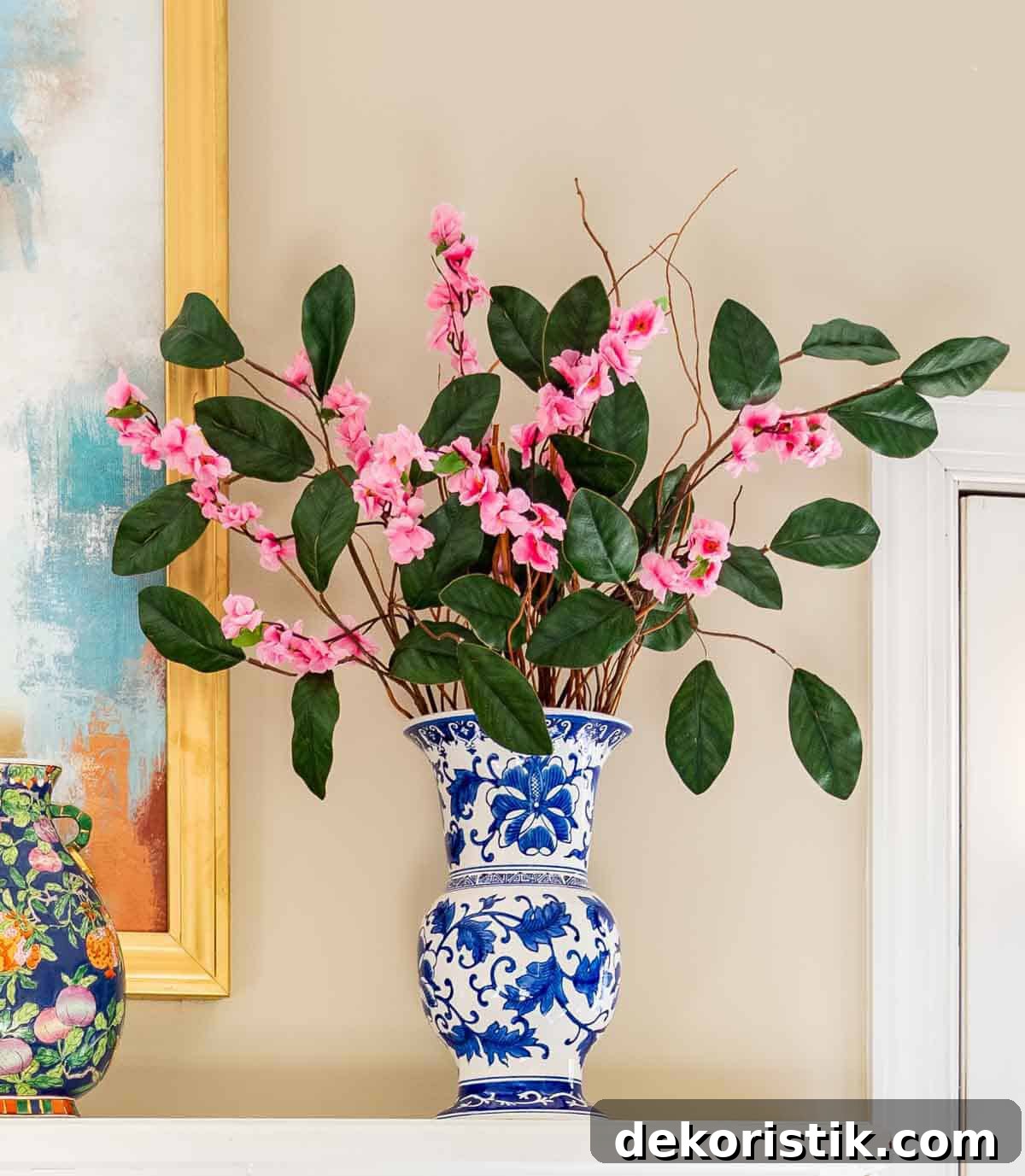 pink faux flower and greenery stems in a tall blue and white vase on a mantel for spring
