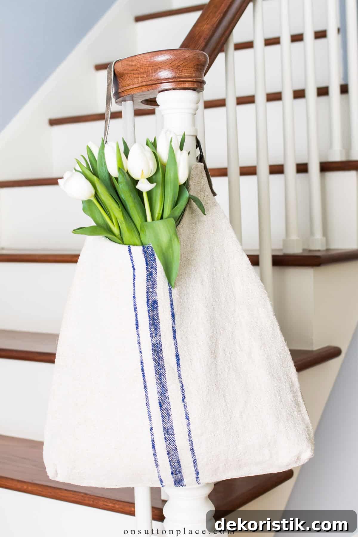 White bag tote back made with grain sack fabric hanging on a newel post with white tulips inside