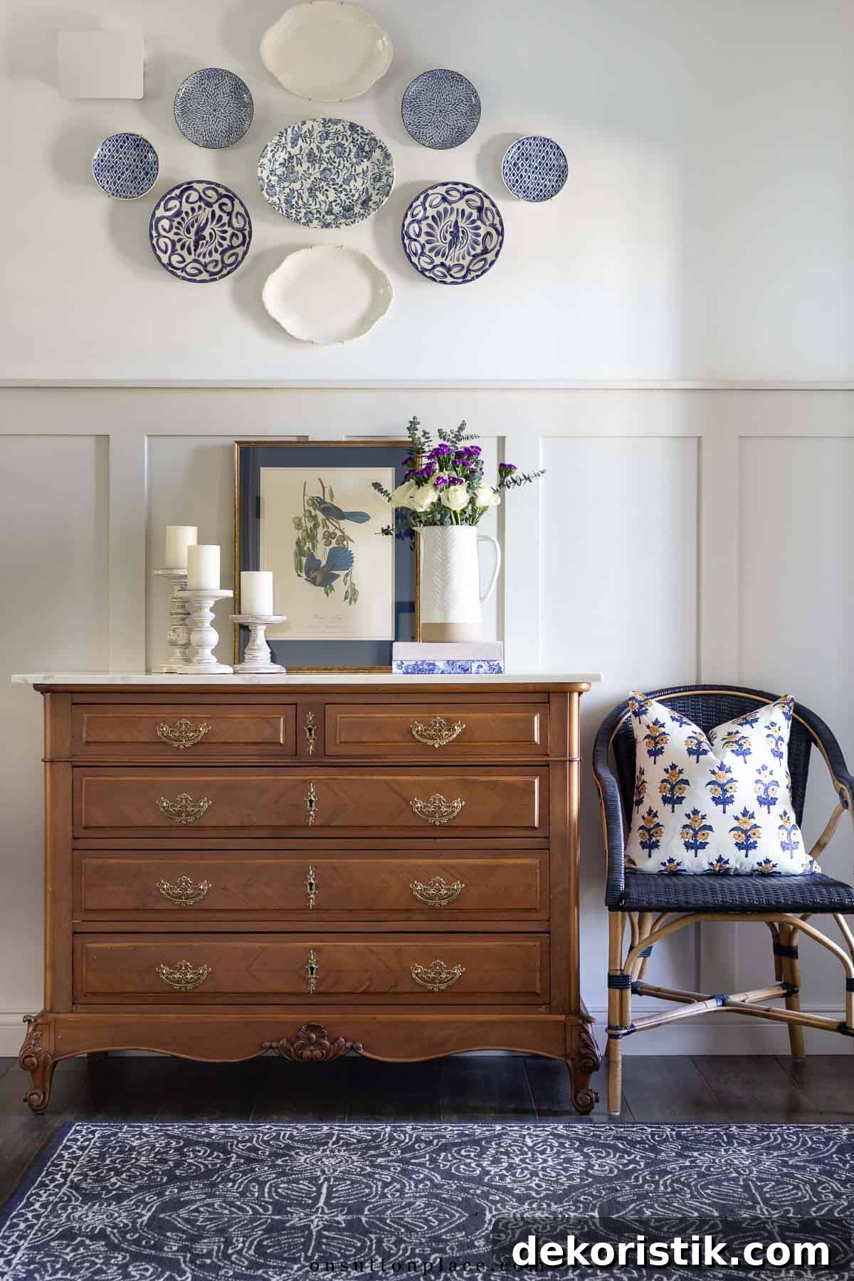 brown chest in front of a board and batten wall with traditional decor on top and a collection of plates hanging on the wall above