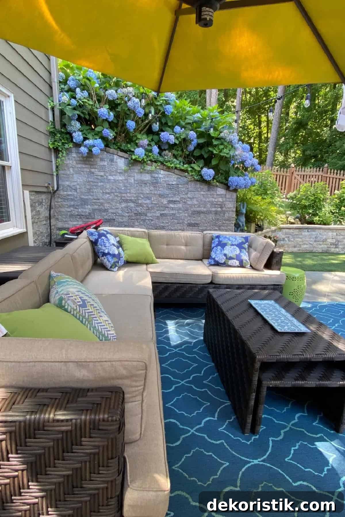 Outdoor patio with a sectional sofa and faux stone wall with hydrangeas spilling over the top