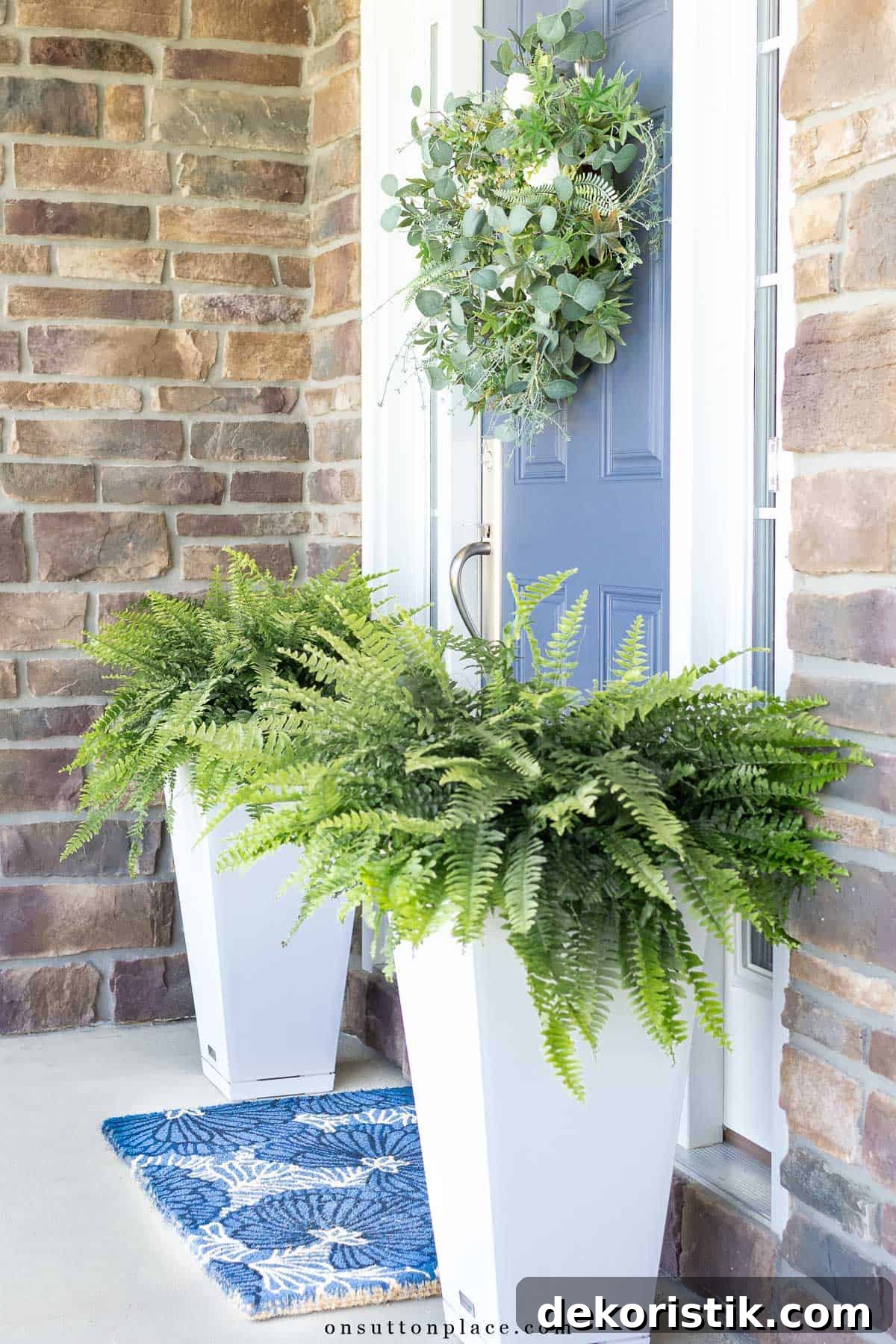 boston ferns in two white tall square planters flanking a blue front door