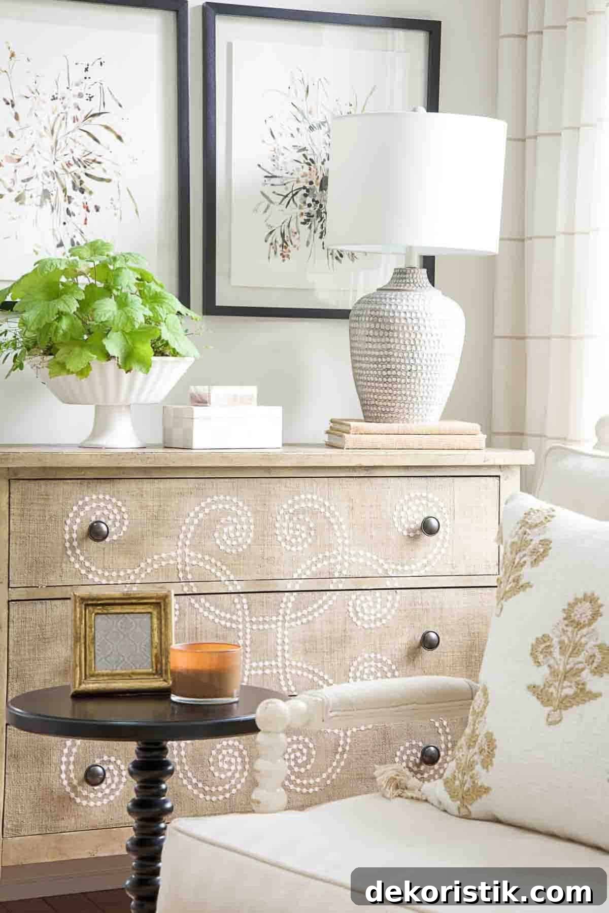 short beige chest with a curlicue design on front with a lamp and white accessories on top