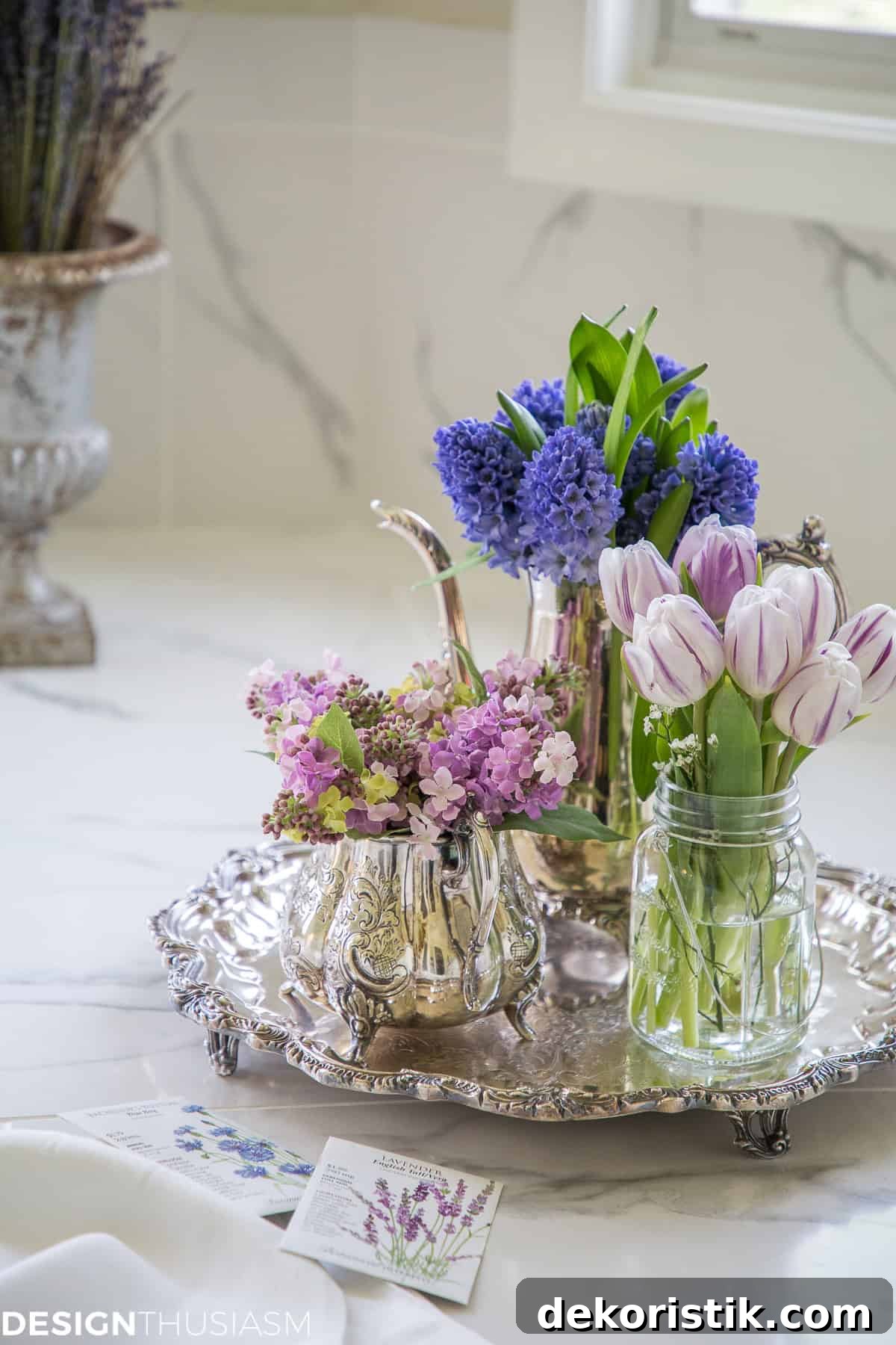 round footed silver tray on a marble bathroom counter holding three vessels filled with lavender colored flowers