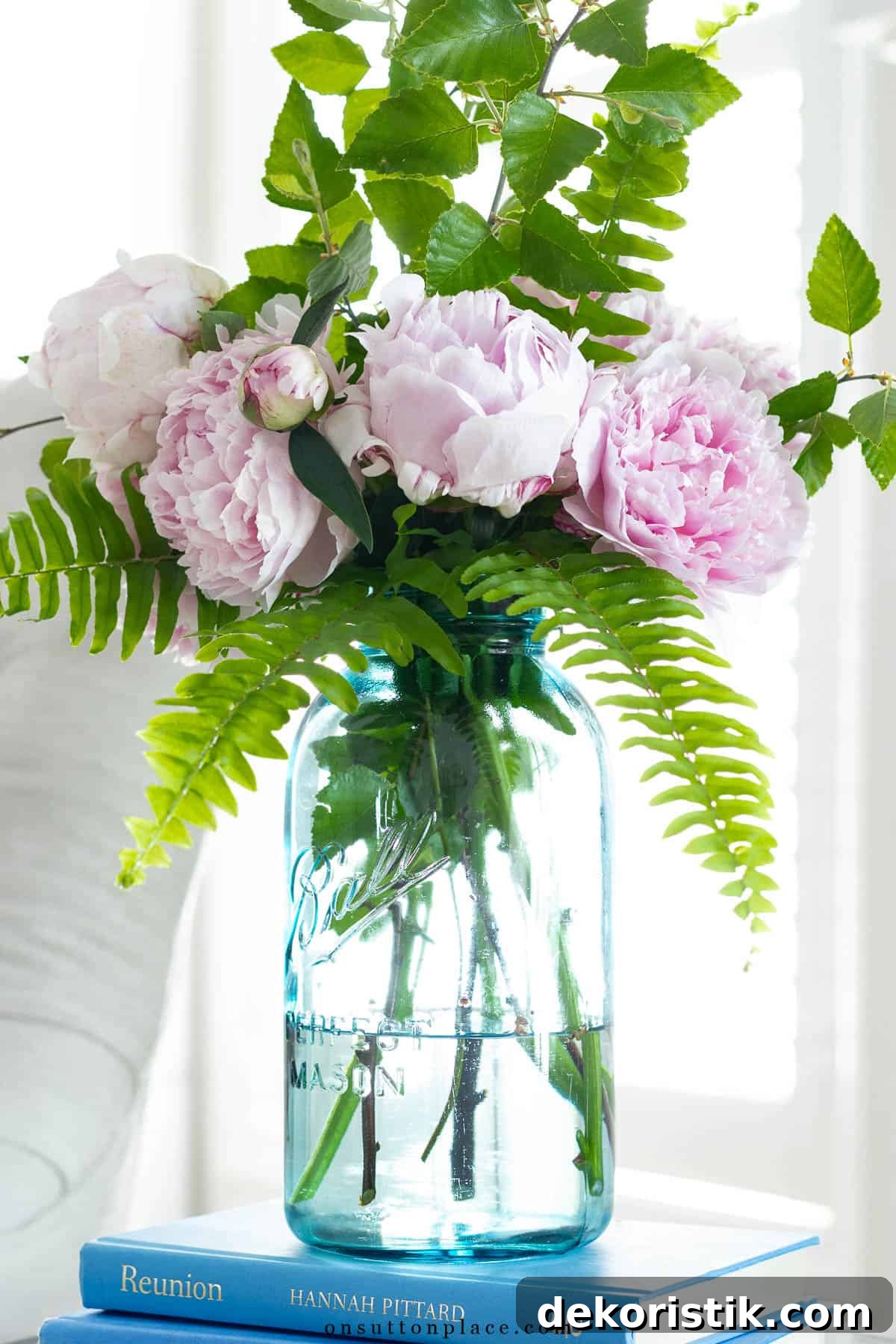 bouquet of pink peonies and fern leaves in an arrangement in a large blue mason jar