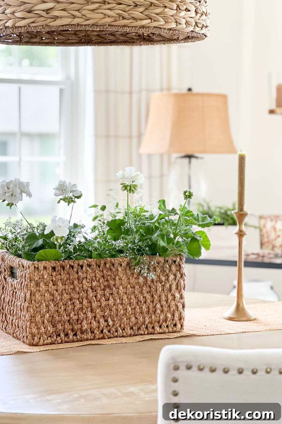 woven basket filled with white geraniums on a kitchen counter with candle and lamp in the background