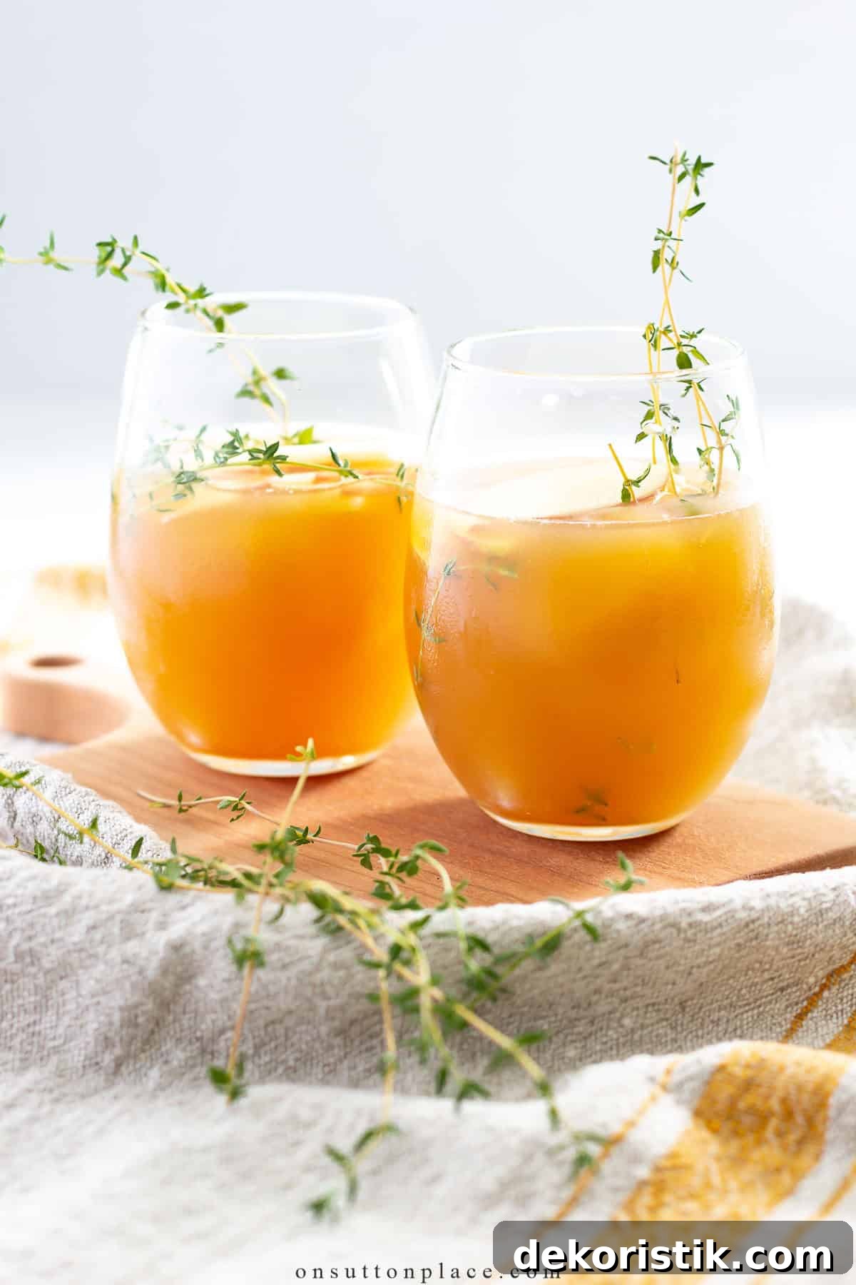 Two stemless glasses filled with a bright orange mocktail garnished for summer