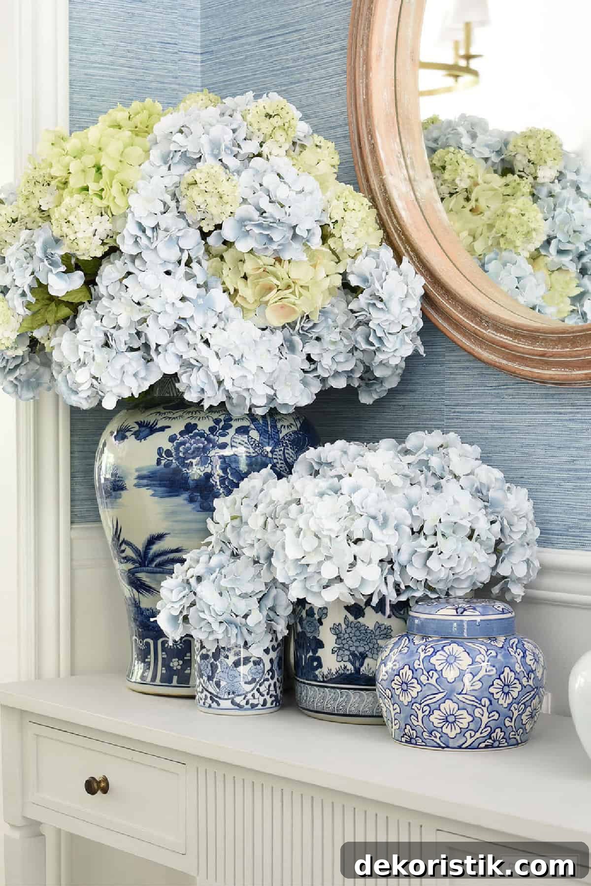 light blue and light green hydrangeas arranged in blue and white chinoiserie containers on a console table in front of a mirror
