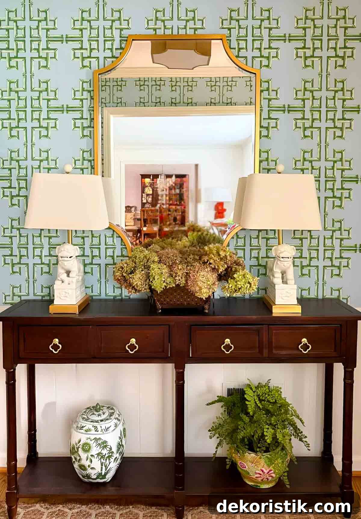Decorative wooden console table with floral arrangements and lamps in front of intricately patterned wall.