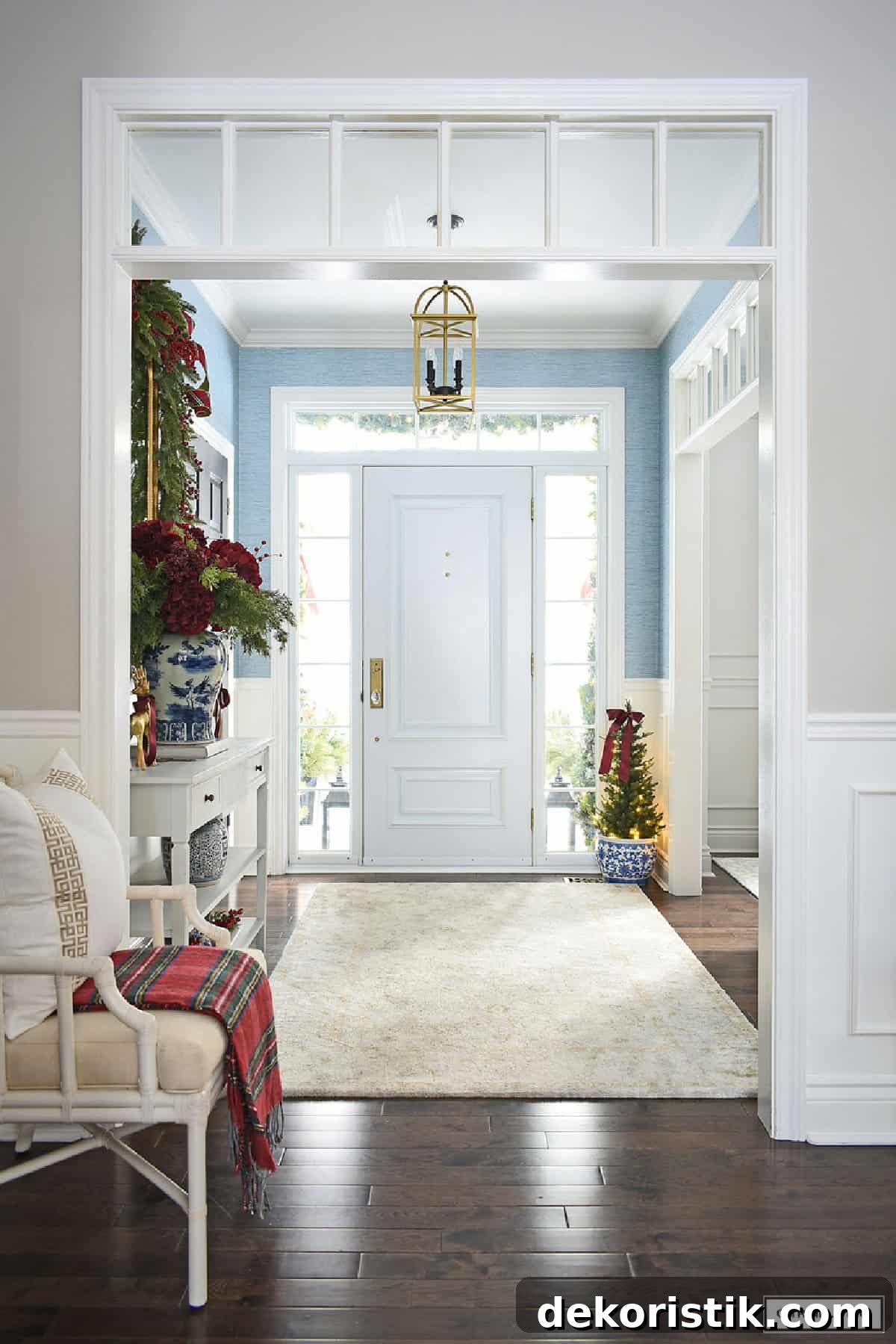 White front door with glass panes and blue wall, entryway decorated for Christmas.