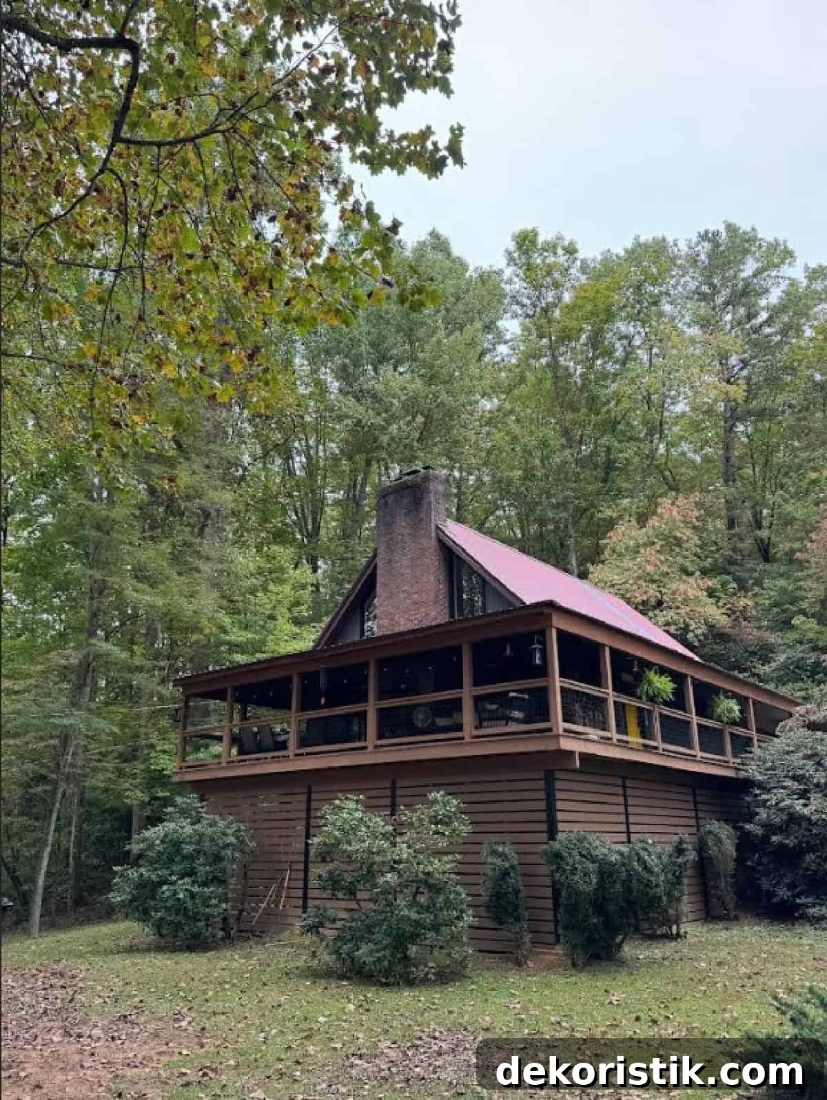 Wooden A-frame cabin surrounded by lush trees in a forest setting.