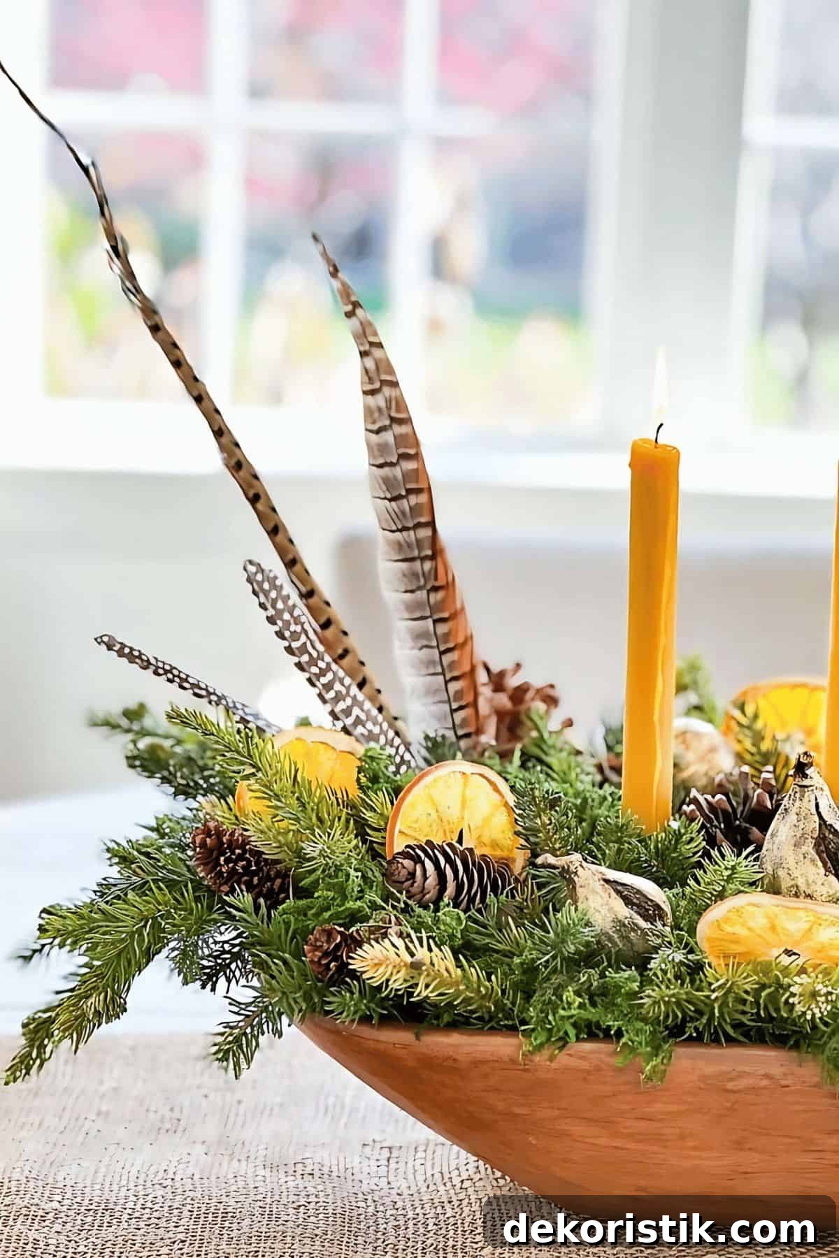 Feathered orange and pinecone centerpiece with candles and dried citrus slices for holiday decor.