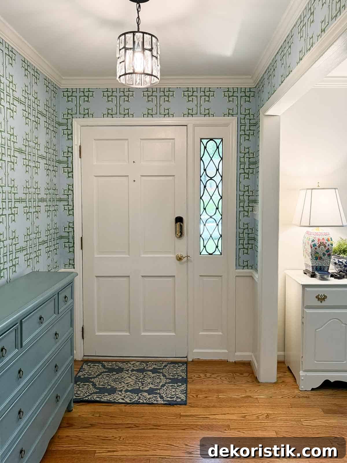 views of a small foyer decorated with chinoiserie accessories, a wood console table, and with blue and green lattice patterned wallpaper