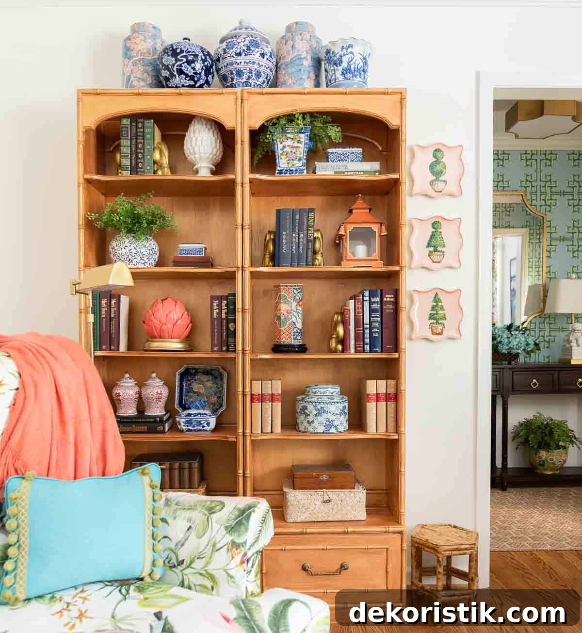 Small Living Room Ideas: How We Made Ours Stylish and Functional 11 partial view of a living room decorated with colorful patterns, chinoiserie accents, and traditional style furniture. Includes a blue velvet loveseat, faux bamboo bookcase, antelope print area rug, samsung frame tv in a gallery wall with art prints, framed needlepoint and plates, with coral accents