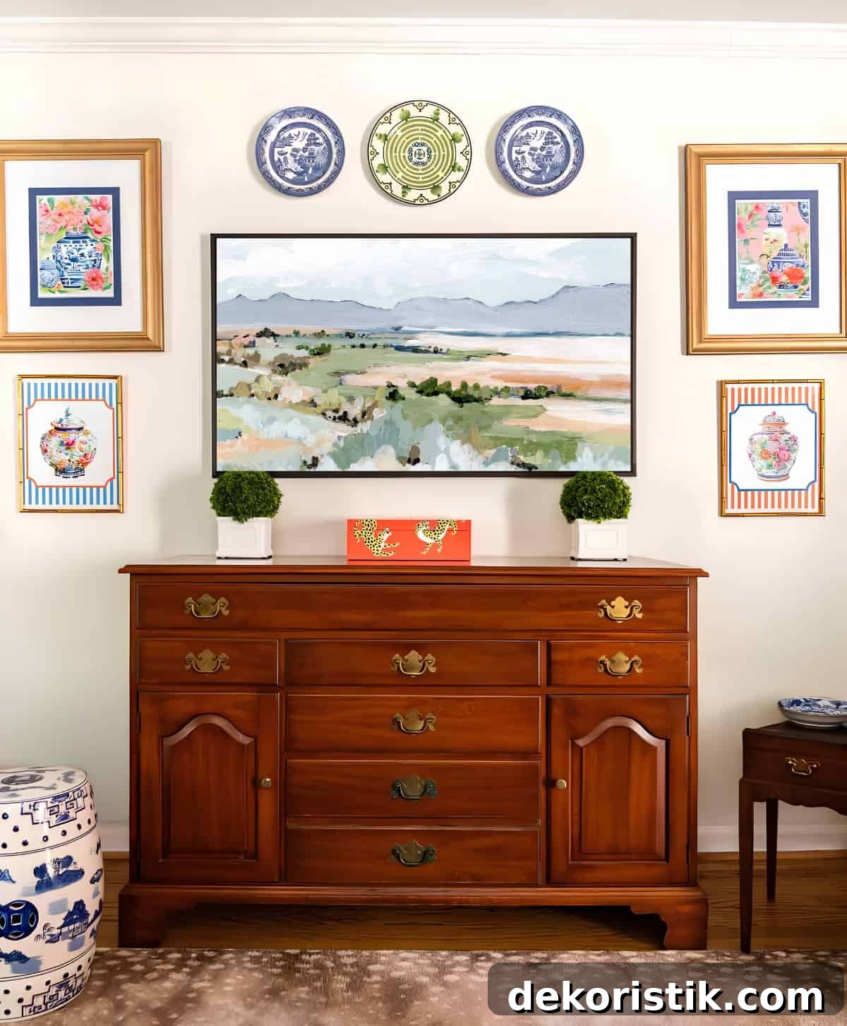 Small Living Room Ideas: How We Made Ours Stylish and Functional 6 partial view of a living room decorated with colorful patterns, chinoiserie accents, and traditional style furniture. Includes a blue velvet loveseat, faux bamboo bookcase, antelope print area rug, samsung frame tv in a gallery wall with art prints, framed needlepoint and plates, with coral accents