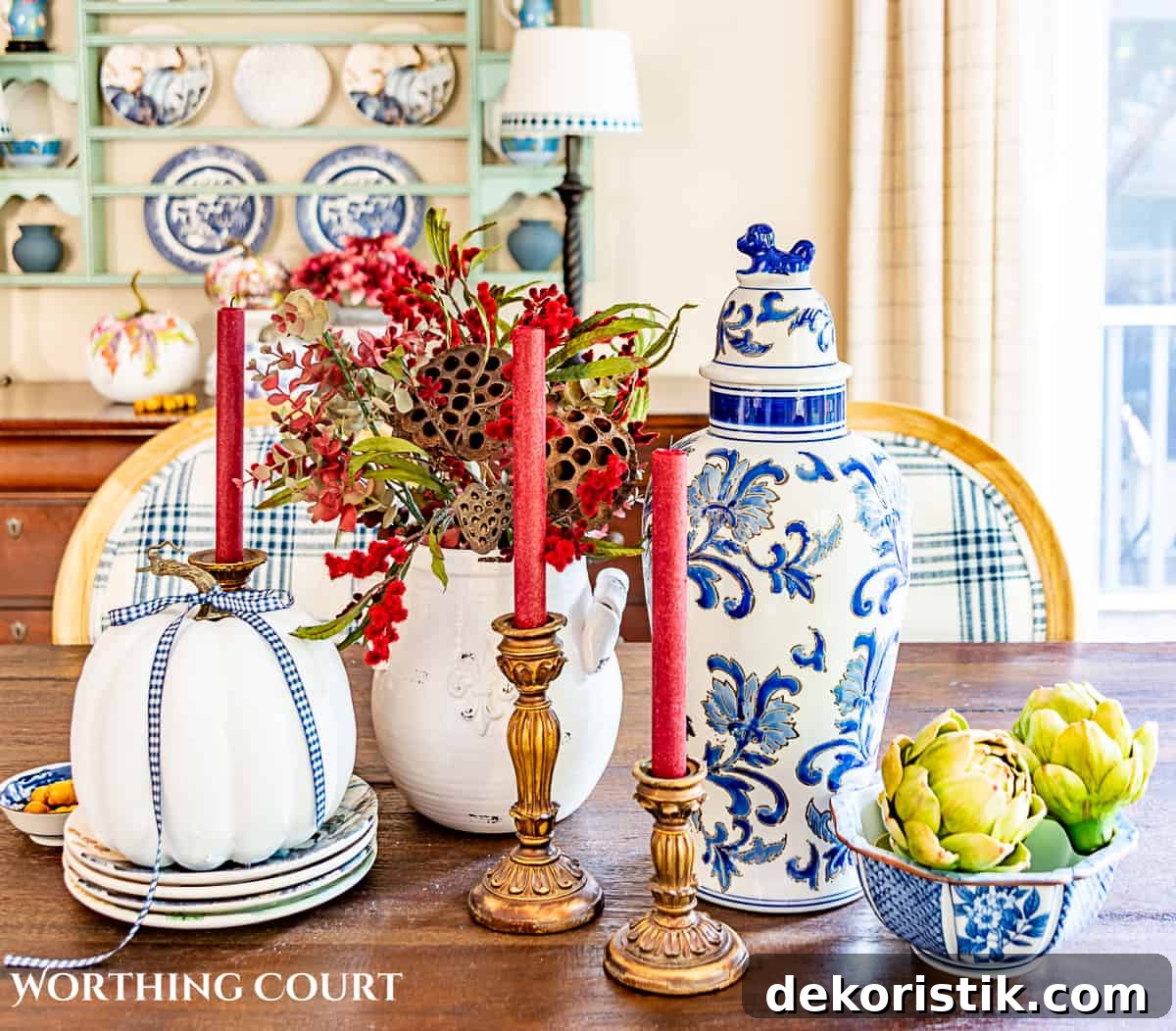 fall centerpiece using blue and white accessories, a white pumpkin, fall colored florals and burgundy candles in gold candle holders