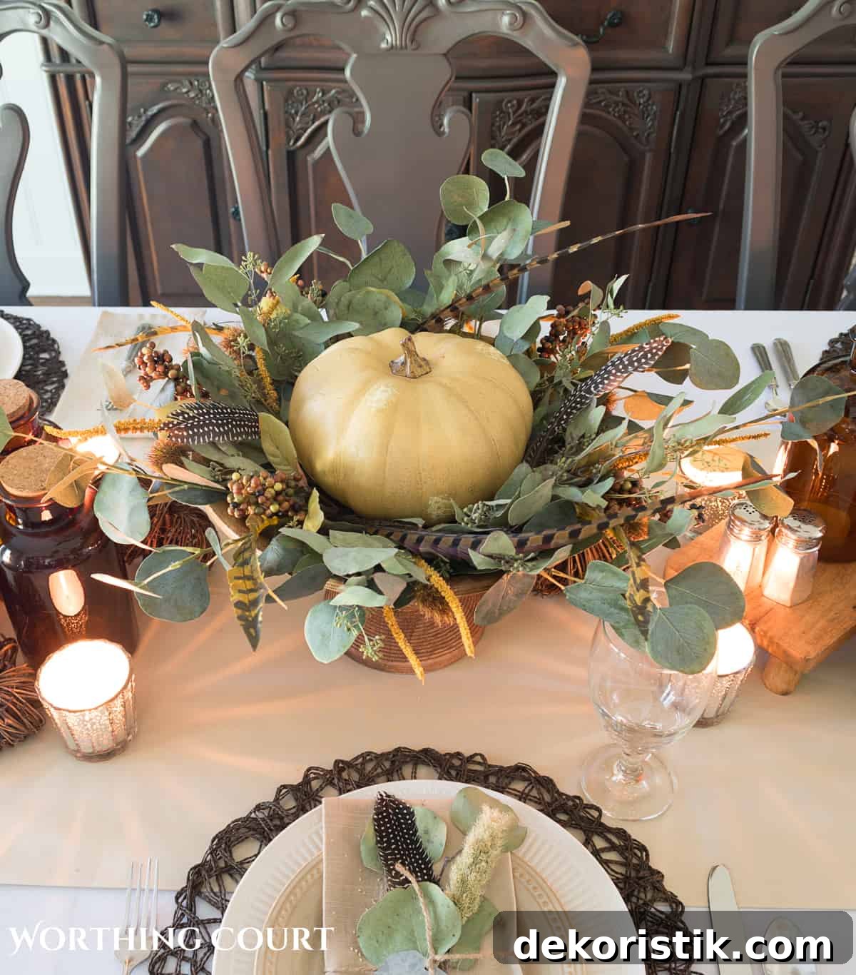 Thanksgiving centerpiece with cream colored pumpkin on a wooden pedestal surrounded by bits of greenery and feathers