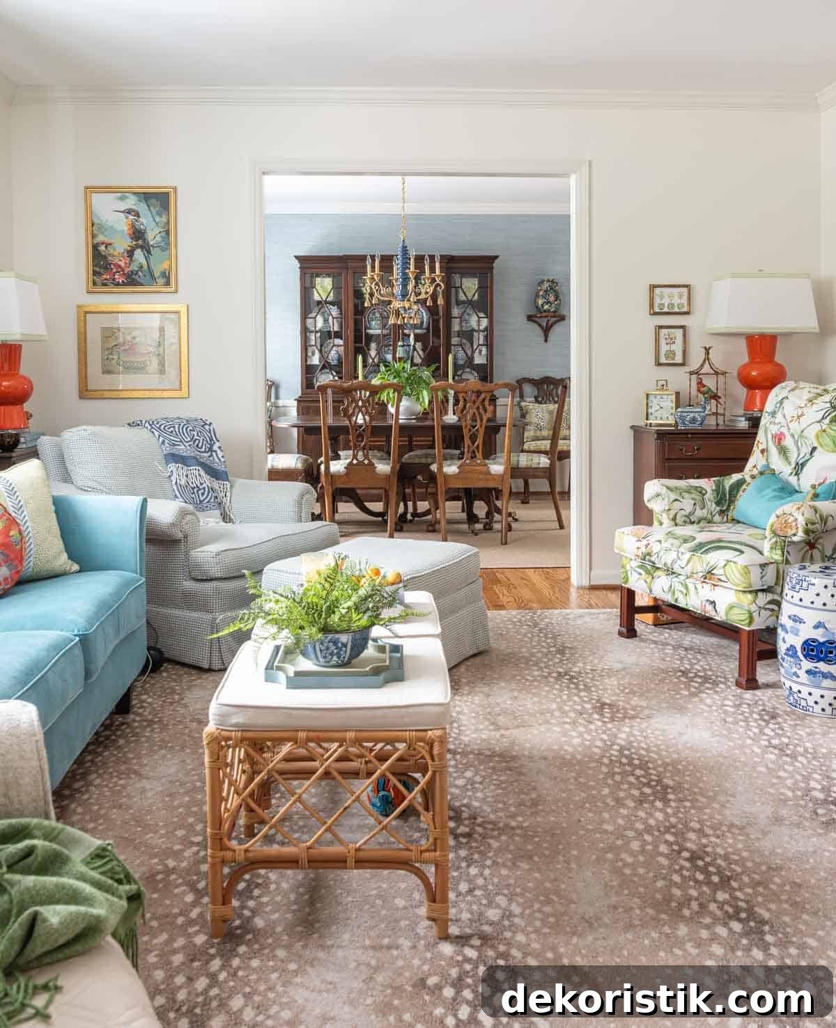 Colorful traditional living room with a blue sofa, floral armchair, rattan coffee table, blue and white accents, and a view into the adjoining dining room.