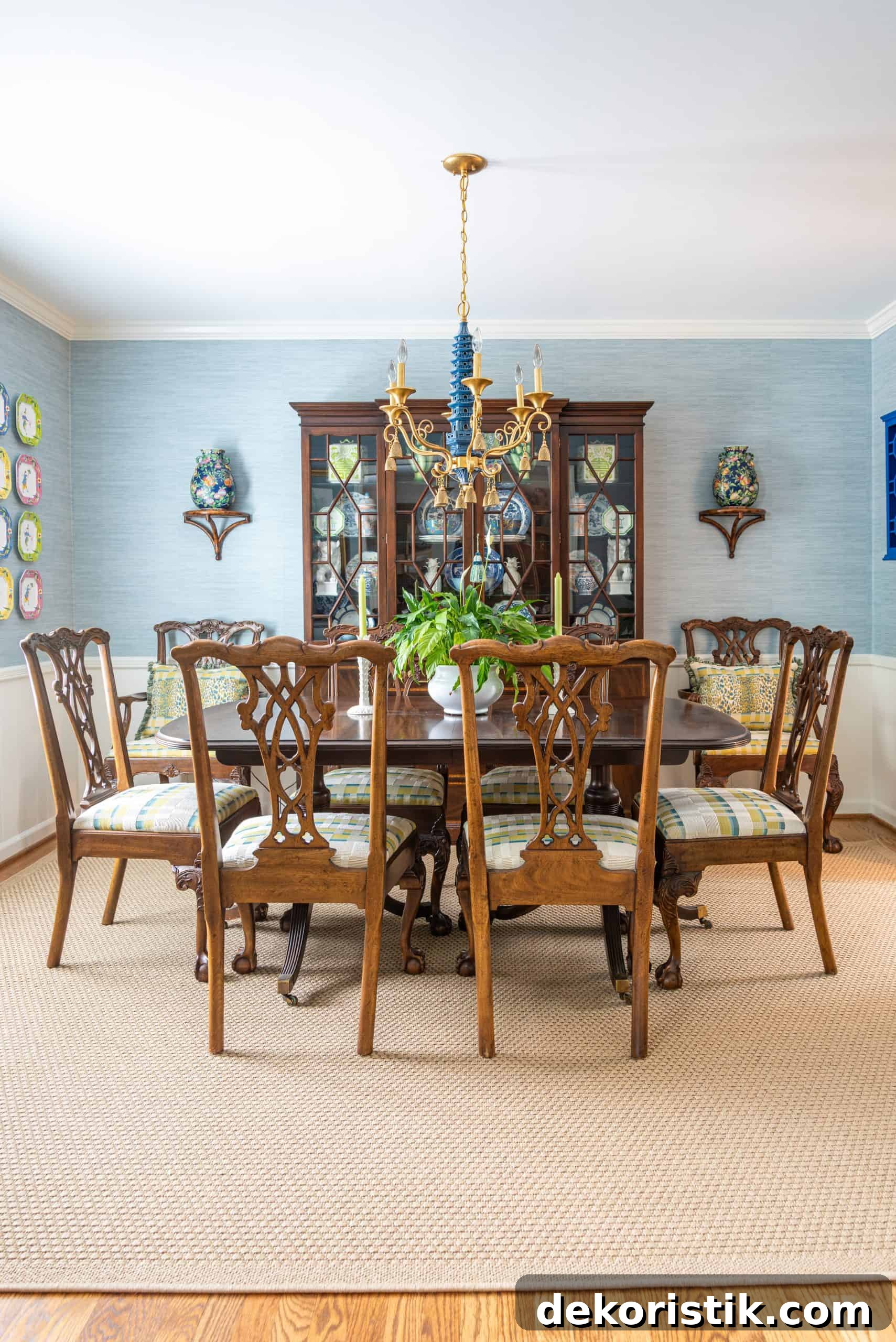 Traditional dining room with blue grasscloth walls, antique wood dining table and chairs, blue and white china, brass chandelier, and colorful chinoiserie accents.