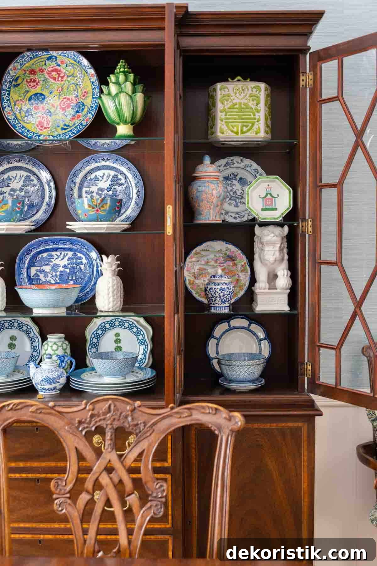 Traditional dining room with blue grasscloth walls, antique wood dining table and chairs, blue and white china, brass chandelier, and colorful chinoiserie accents.