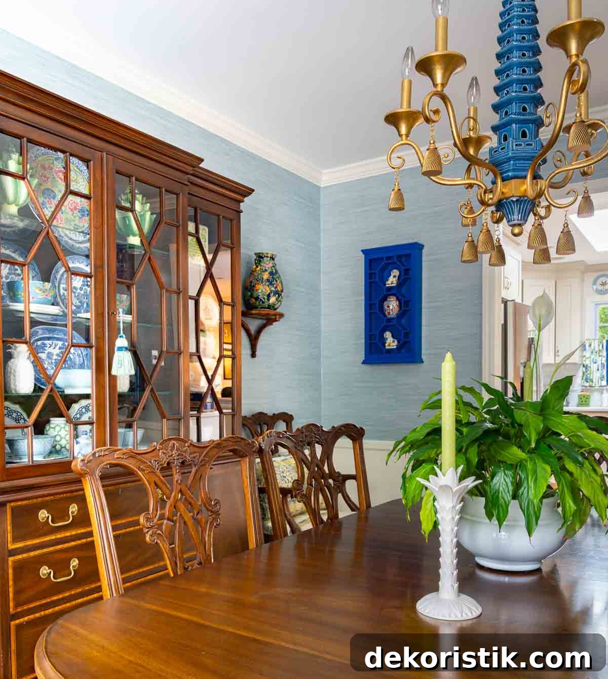 Traditional dining room with blue grasscloth walls, antique wood dining table and chairs, blue and white china, brass chandelier, and colorful chinoiserie accents.