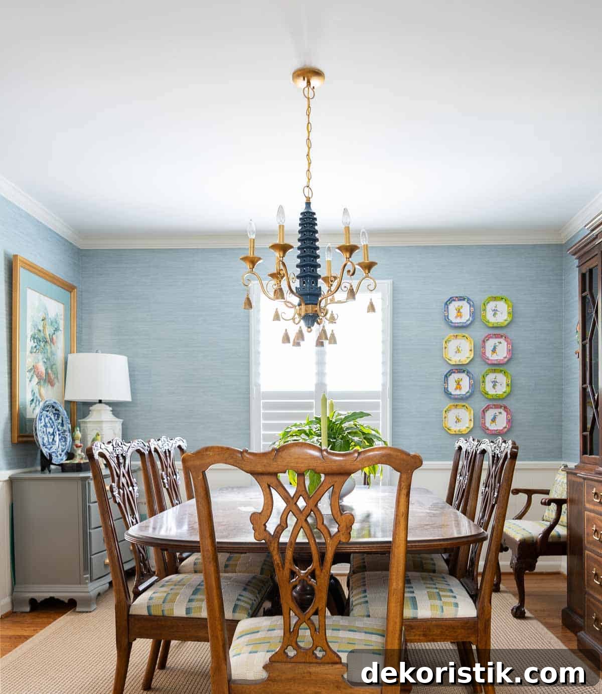 Traditional dining room with blue grasscloth walls, antique wood dining table and chairs, blue and white china, brass chandelier, and colorful chinoiserie accents.